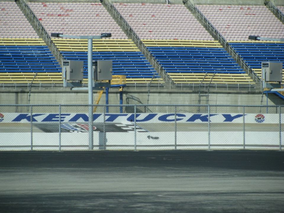 Grandstands with blue and yellow seats overlook a race track with a "KENTUCKY" banner