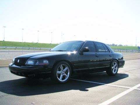 2003 Mercury Marauder - A black 2003 Mercury Marauder is shown from a three-quarter front view, parked in a lot with a racetrack in the background.