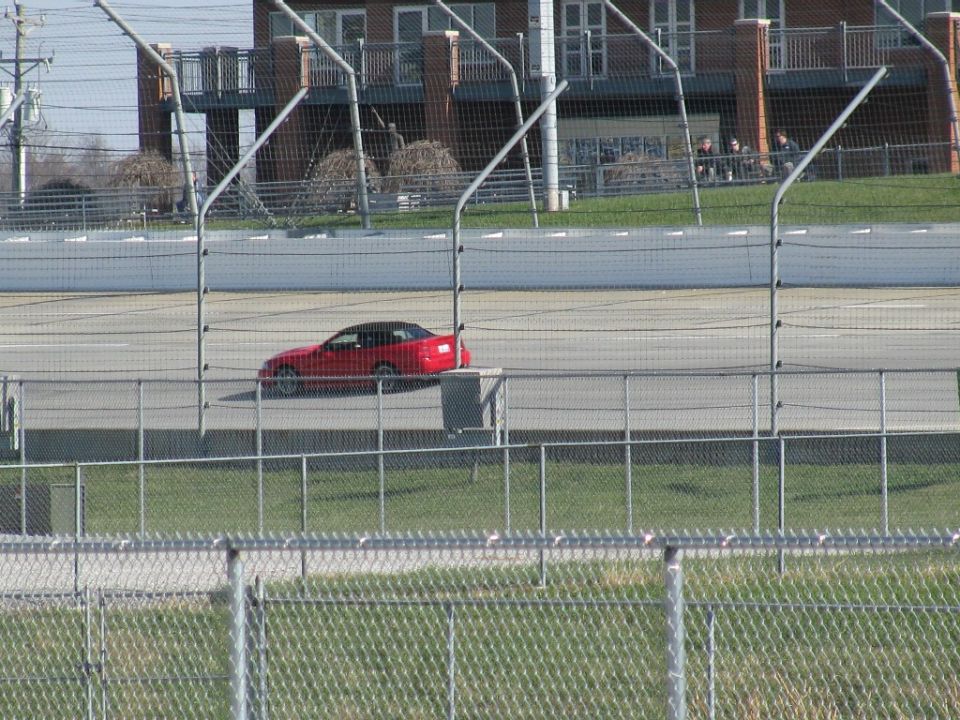 Red coupe with black roof on a racetrack, viewed from the side