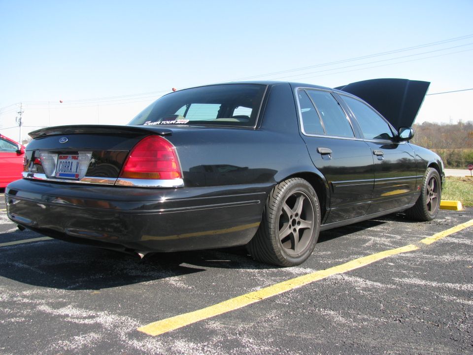 In the parking lot, a rare Bondurant "Cobra Vic".

"This Crown Victoria Police Interceptor (Cobra Vic) is one of eighteen cars commissioned by Ford and built by Roush Industries for the world famous Bob Bondurant School of High Performance Driving. This is not only a unique and highly desirable car it is probably where the idea for the Marauder originated. The Cobra Vic's were used as instructor cars for the school and are highly modified for safety and performance. Some of the modifications include a 4.6L 4V Mustang Cobra engine, 5 speed manual transmission, custom Cobra gauges, exterior vehicle appearance enhancements, 6-point roll cage, fuel cell etc..... Own a piece of Bob Bondurant History.


1999 Police Interceptor Crown Victoria

ENGINE: 1999 SVT Mustang Cobra 4.6L 4V.
320 HP.
Full length Cobra windage tray with modified Mark VIII oil pan.
Emissions controls removed.
Custom Bondurant engine calibration.
Custom H â€“ pipe with catalytic converters removed.
Borla custom dual exhaust system.
Custom cooling system including production 6.8L V10 water pump and radiator, engine driven fan with custom shroud and an 18â€ electric cooling fan.
1995 SVT Mustang Cobra R engine oil cooler.
Battery relocated to trunk.

WEIGHT: 4,800 Lbs.

TRANSMISSION/ 1999 SVT Mustang Cobra T-45 5 speed with carbon fiber blocking rings.
DRIVETRAIN: B & M Ripper Shifter.
Custom steel drive shaft with safety loop.
3.73:1 axle ratio with production limited slip.

FUEL SYSTEM: Custom 22 gallon racing fuel cell.
1999 SVT Mustang Cobra fuel pump.
Custom stainless steel and braided fuel lines 

SUSPENSION: Front:
Eibach 1000 lb per inch springs.
Monroe Shocks with custom calibration.
Winston Cup style 2â€ diameter solid front sway bar with custom links.
Modified alignment settings:
Camber 1.8 degrees negative
Caster 7.0 degrees positive
Toe 0.0 degrees.

Rear:
Eibach 160 lb per inch springs.
Monroe shocks with custom calibration.
Production .708 diameter solid sway bar.
Production Watts linkages.

BRAKES: Production Crown Victoria disk brakes.
Performance Friction 90 compound race brake pads.
Baer Brakes custom steel braided brake lines.
Custom brake cooling ducts.

WHEELS/ 1995 SVT Mustang Cobra R 17 X 9â€ wheels.
TIRES : Goodyear Eagle HP Ultra 275/40/R17.

INTERIOR: 1999 SVT Mustang Cobra instrument cluster.

Four point safety harnesses at all four seating locations.
Six point fully integrated Roush roll cage"