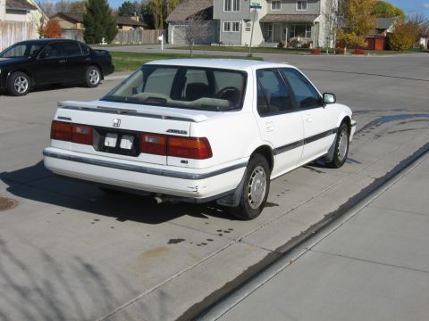1989 Honda Accord - A white 1989 Honda Accord sedan is seen from the rear three-quarter angle, with a black sedan parked behind it.