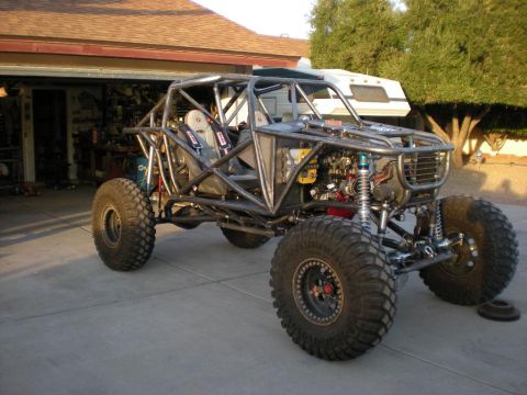 2009 Suzuki Samurai - Custom tube frame buggy with large off-road tires and racing seats, parked in a driveway with a trailer and garage in the background.