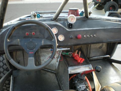 Suzuki Samurai - Interior view of a stripped-down custom off-road buggy showing a bare metal dash with multiple round gauges, a black 'Grant' three-spoke st…