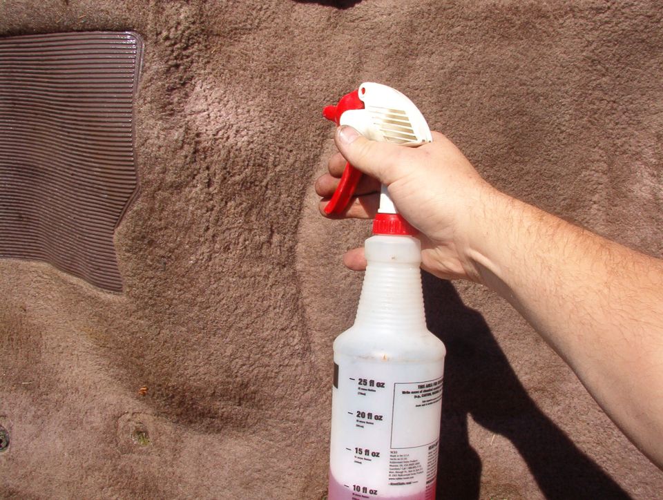 Hand holding a spray bottle of cleaner against brown carpet