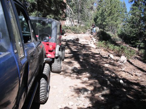 1991 Ford Bronco - Two off-road vehicles navigate a challenging, rocky path through a wooded mountainside.