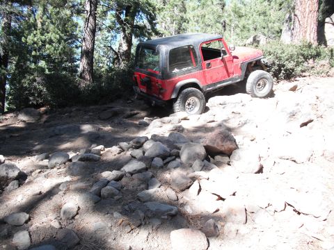 1991 Ford Bronco - A red Jeep Wrangler navigates a challenging rocky path in a wooded area.