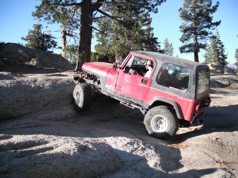 1991 Ford Bronco - A red Jeep Wrangler navigates a rocky off-road trail under a clear blue sky.