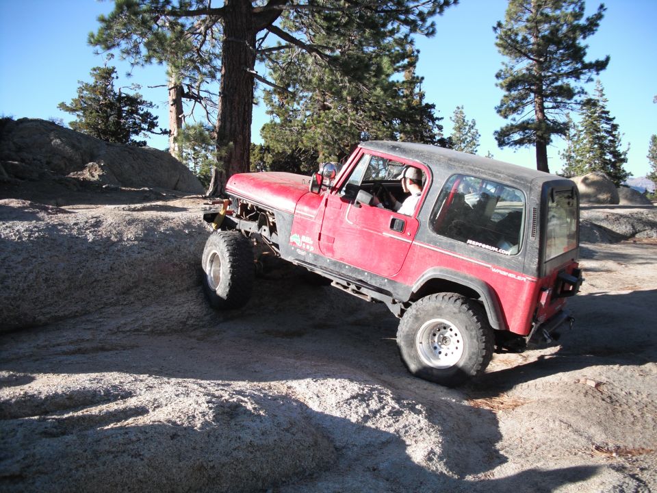 Red Jeep Wrangler climbing over rocks on a trail. Driver visible