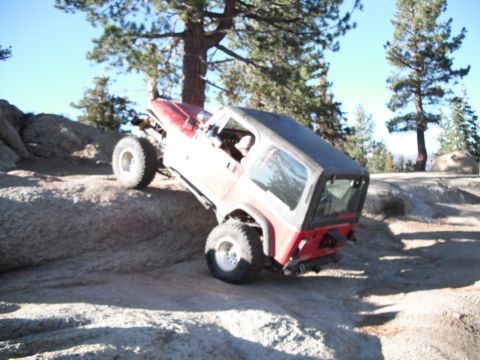 1991 Ford Bronco - A red Jeep Wrangler navigates a challenging rocky terrain on a sunny day.