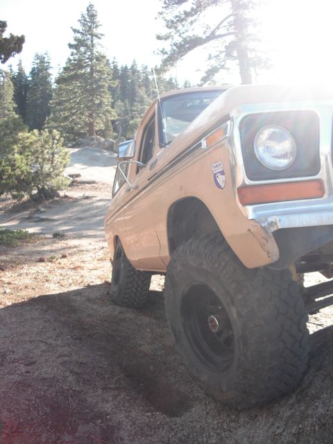 1991 Ford Bronco - A tan pickup truck with large off-road tires is parked on a dirt trail surrounded by trees.