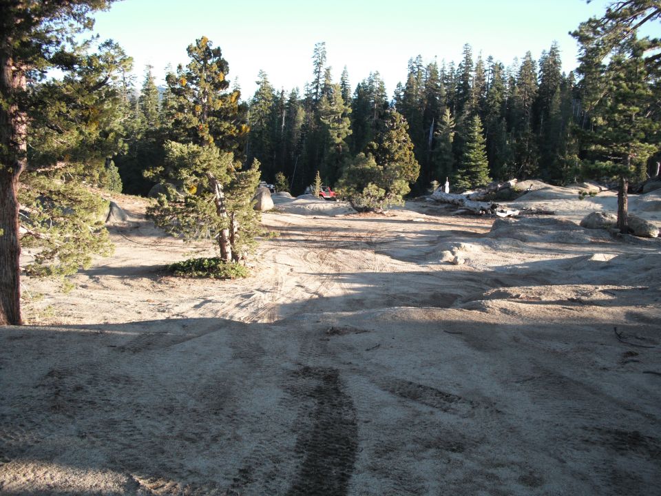 Red off-road vehicle parked in a wooded, rocky area with tire tracks on the ground