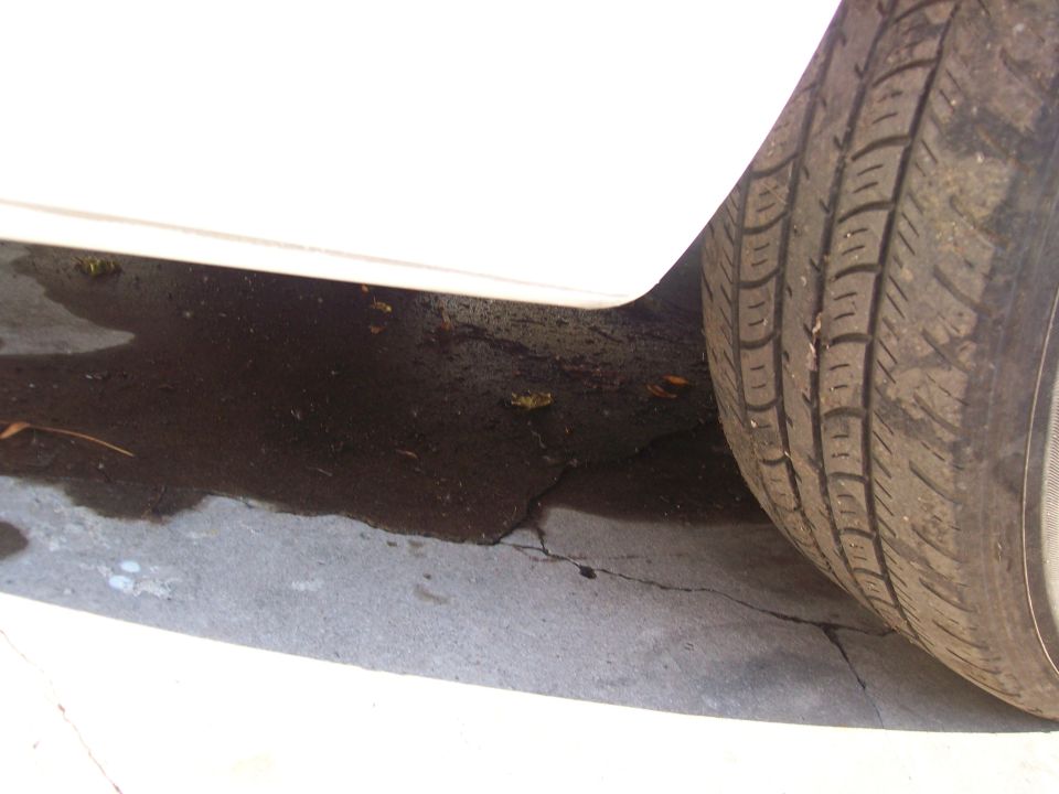 Close-up of a tire and a puddle on the ground next to a white car's lower body panel