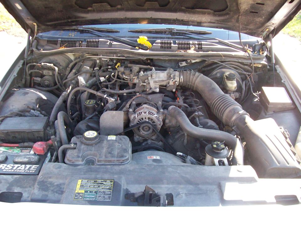 Engine bay of a 2004 Ford Crown Victoria. Shows the V8 engine, air intake, battery, and coolant reservoir