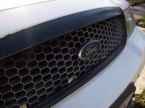 2004 Ford Crown Victoria - Close-up of a white Ford Crown Victoria's front grille, showing the honeycomb design and Ford emblem.