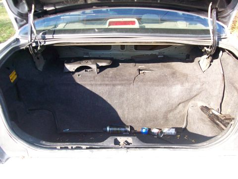 2004 Ford Crown Victoria - The trunk of a 2004 Ford Crown Victoria is shown, appearing empty except for some discarded cans and a tool.