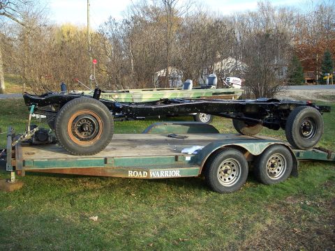 1979 Ford F-250 - A bare truck chassis is transported on a trailer, with a boat visible in the background.