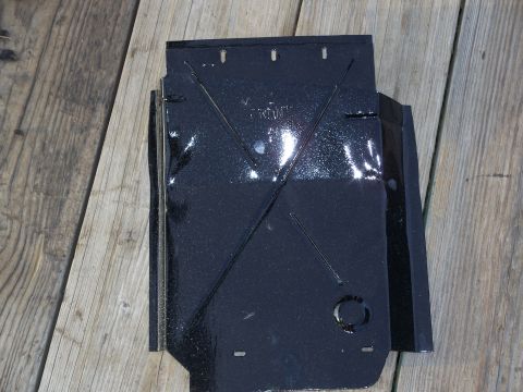 1979 Ford F-250 - A black metal part, possibly a skid plate, with embossed lines and the word "FRONT" visible, resting on a wooden surface.