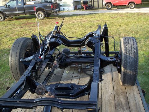 1979 Ford F-250 - The bare frame of a truck sits on a wooden trailer, with two other trucks visible in the background.
