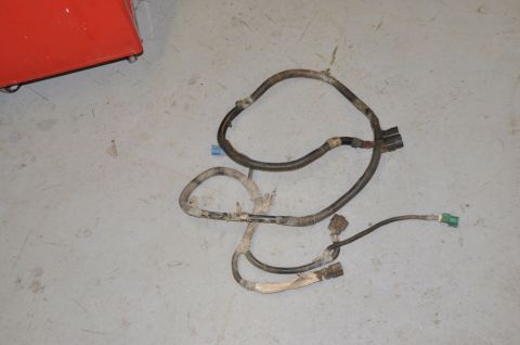 1996 Ford Bronco - A dirty wiring harness with multiple connectors lies on a concrete surface next to a red object.