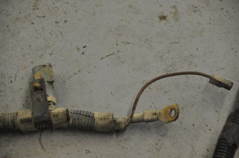1996 Ford Bronco - A close-up view of a worn automotive wiring harness, showing a rusty ground strap and connector.