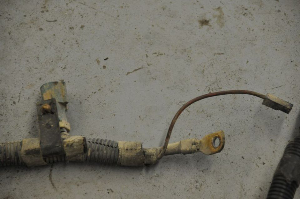 Close-up of a dirty automotive wiring harness with a rusty ground strap and connector