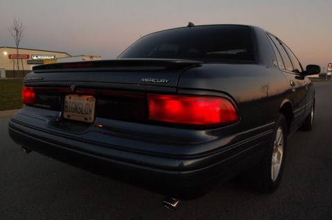 1985 Mercury Grand Marquis - Rear view of a dark sedan with a spoiler and a custom license plate reading 'SIGNSLOW'.