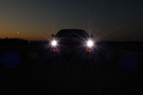 1985 Mercury Grand Marquis - A car's headlights shine brightly against the twilight sky.