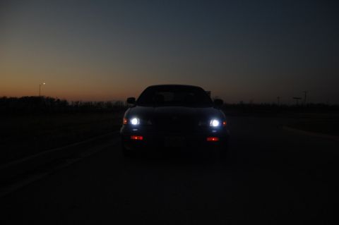 1985 Mercury Grand Marquis - Car's headlights illuminate the road as dusk settles.