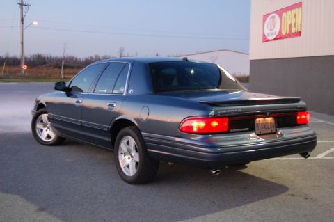 1985 Mercury Grand Marquis - The rear of a Mercury Grand Marquis is shown parked next to a building with an 'OPEN' sign.