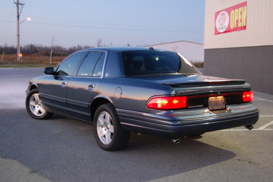 Dark blue Mercury Grand Marquis, rear view, parked near a building with an open sign