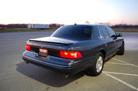 1985 Mercury Grand Marquis - This dark blue sedan, likely a 1998 Mercury Grand Marquis, is viewed from the rear 3/4 angle.