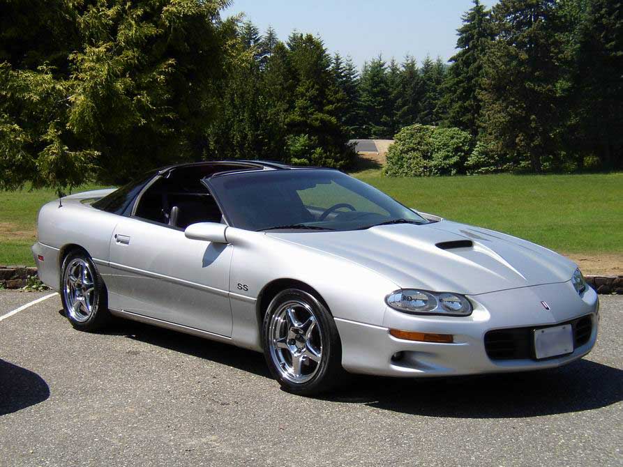 Silver Chevrolet Camaro SS T-top coupe parked on pavement in front of evergreen trees
