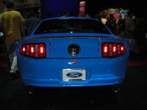1998 Ford Crown Victoria - Rear view of a blue Ford Mustang, a prominent spoiler and the Ford logo on the license plate. The taillights are illuminated.