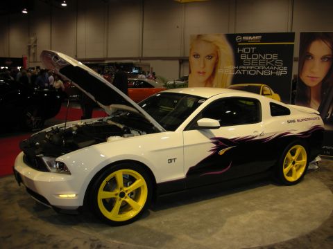 1998 Ford Crown Victoria - White Ford Mustang GT with custom graphics and yellow wheels is displayed with its hood open.