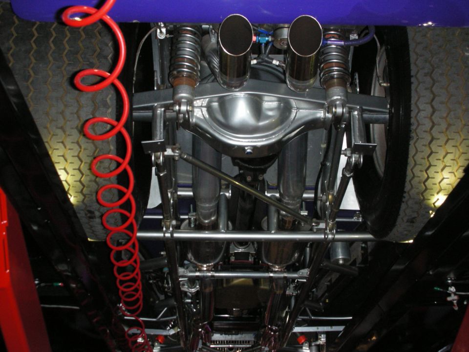 Underside view of a custom hot rod's rear axle, dual exhaust pipes, and suspension components