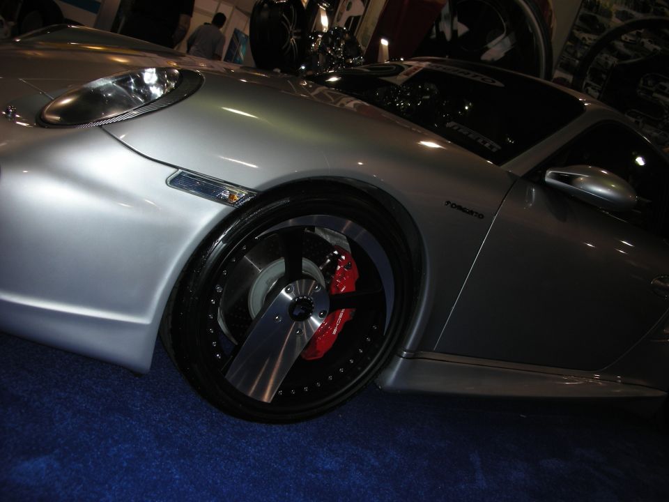 Silver sports car with custom wheels and red brake calipers, viewed from the front quarter