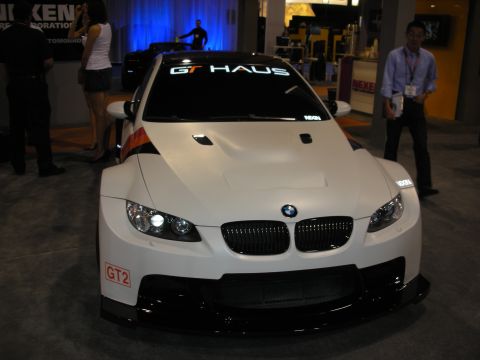 1998 Ford Crown Victoria - A white BMW M3 GT2 race car is displayed indoors, a prominent GT HAUS banner on the windshield.