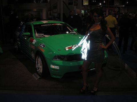 1998 Ford Crown Victoria - Green Ford Mustang race car with Formula Drift decals, parked indoors next to a woman.