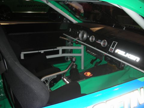 1998 Ford Crown Victoria - The interior of a race car shows a roll cage, racing seat, and dashboard with gauges and Falken branding.