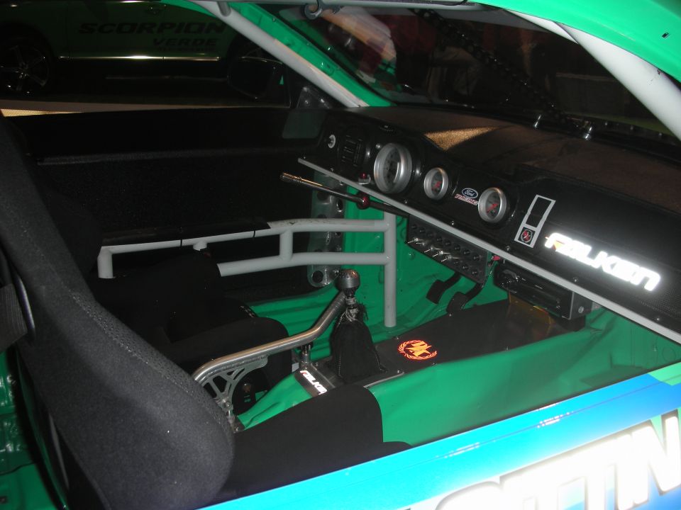 Interior of a race car with a roll cage, racing seat, and Falken branding on the dashboard