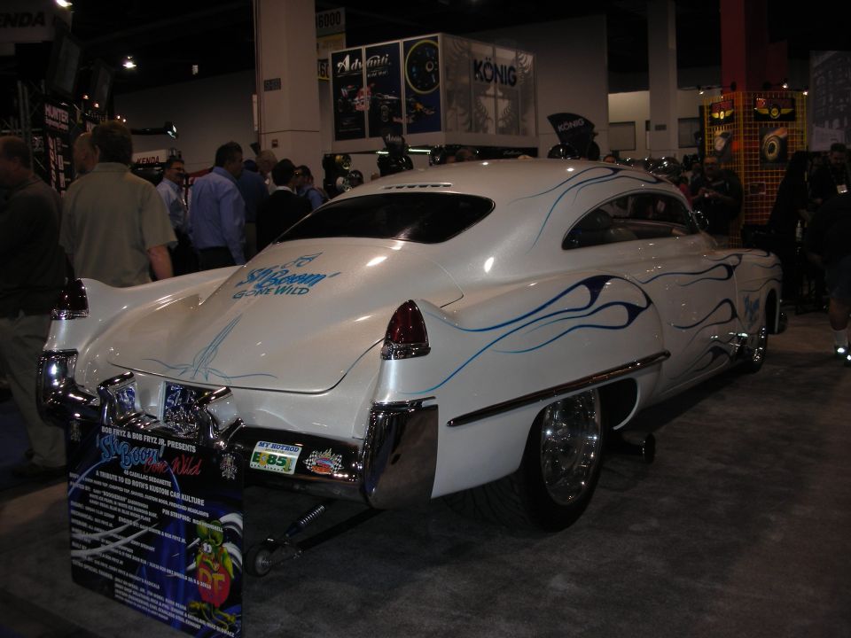 White custom coupe with blue flames and a sign that reads 'S'Boom Gone Wild'