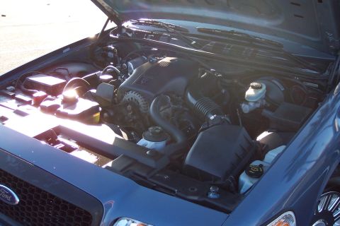 2001 Ford Crown Victoria - The engine bay of a blue 2001 Ford Crown Victoria is shown with the hood open, revealing the engine components.