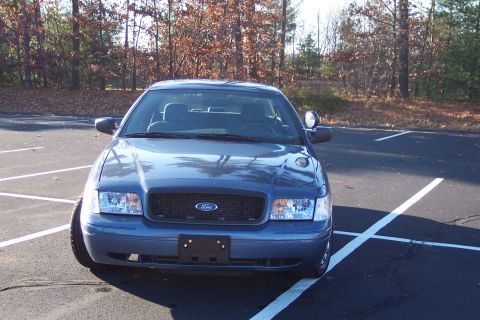 2001 Ford Crown Victoria - A blue 2001 Ford Crown Victoria is parked in a parking lot with trees in the background.