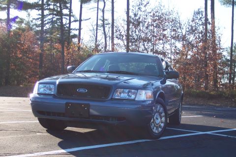 2001 Ford Crown Victoria - A dark blue 2001 Ford Crown Victoria is parked in an outdoor lot with trees in the background.