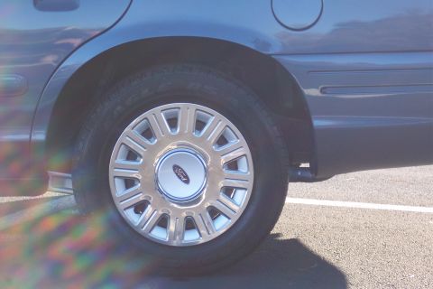 2001 Ford Crown Victoria - The rear wheel and fender of a dark blue 2001 Ford Crown Victoria are visible.
