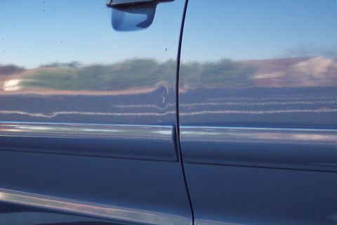 2001 Ford Crown Victoria - The side of a car shows a distorted reflection of the sky and surrounding landscape.