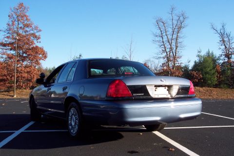 2001 Ford Crown Victoria - A blue Ford Crown Victoria is parked in a lot on a clear day, with trees in the background.