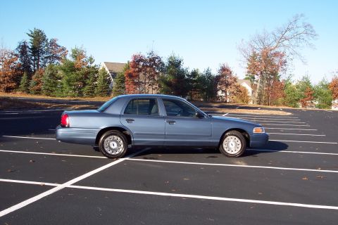 2001 Ford Crown Victoria - A blue 2001 Ford Crown Victoria sedan is parked in an empty lot on a clear day.