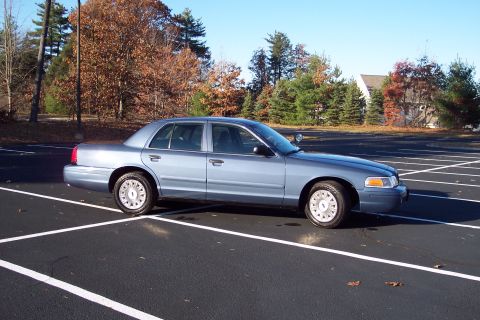 2001 Ford Crown Victoria - A light blue 2001 Ford Crown Victoria sedan is parked in an empty lot on a clear day.