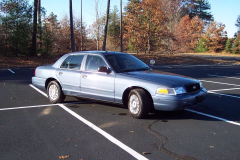 2001 Ford Crown Victoria - A blue 2001 Ford Crown Victoria is parked in an empty lot on a sunny day.